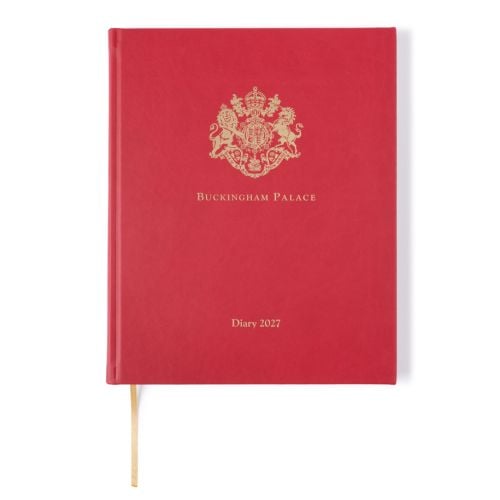 Closed Buckingham Palace 2027 diary with a red cover. A gold royal Coat of Arms crest is embossed at the top, with “Buckingham Palace” printed beneath and “Diary 2027” centred near the bottom. A gold ribbon bookmark extends from the base.