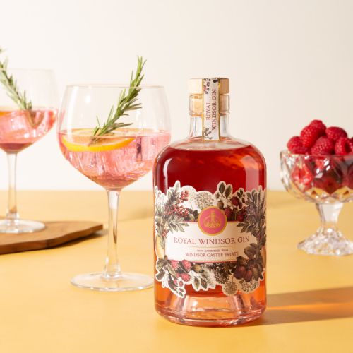 Front of pink gin bottle. Clear glass bottle with cork stopper. Label is illustrated with botanicals and flowers that are included in the drink.