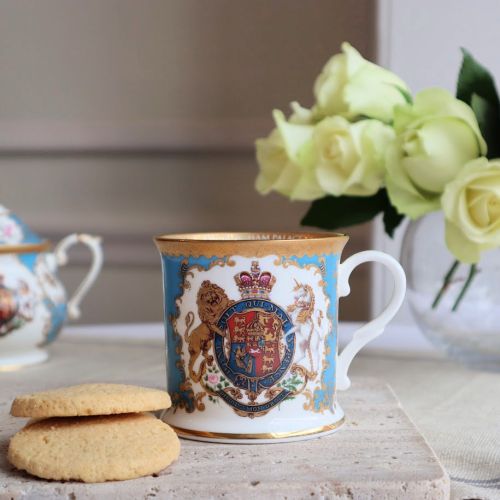 Royal coat of arms fine bone china tankard featuring a lion and unicorn royal crest surrounded by ornated gold patterns and flower patterns on a light blue coloured background. Gold plated with the words Buckingham Palace, Windsor Castle and Palace of Hol