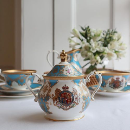 Royal coat of arms English fine bone china sugar bowl featuring a lion and unicorn royal crest surrounded by ornated gold patterns and English flower patterns on a turquoise blue coloured background. The lid is topped with with a royal gold crown. 