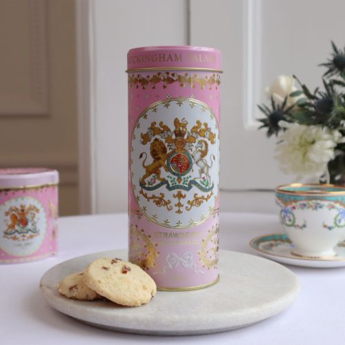 pink biscuit tin with the crest at the centre of the tin. Stood next to a few biscuits
