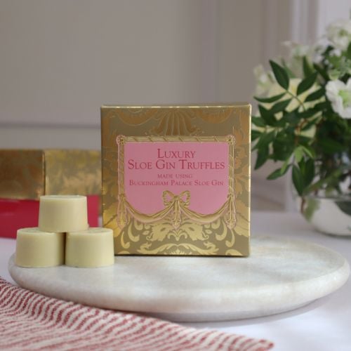 A golden patterned box with a pink centre with dark pink text, with "Luxury Sloe Gin Truffles, nade using Buckingham Palace Sloe Gin" in writing. 