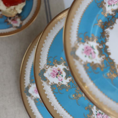 A three tier cake stand, featuring three turquoise plates with floral design and gold detailing. 