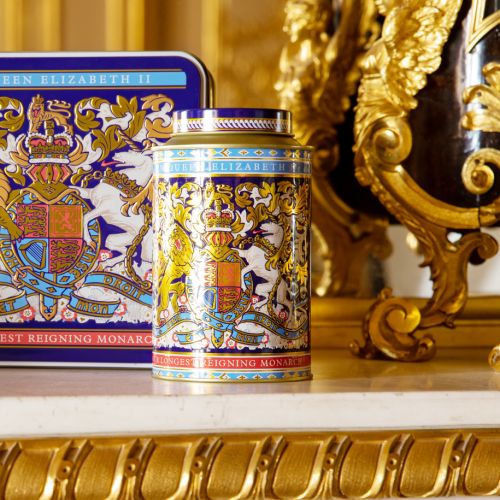 Round tin with the lion and unicorn design at the centre. The lid and edges of the tea caddy are in a gold, purple and light blue design. 