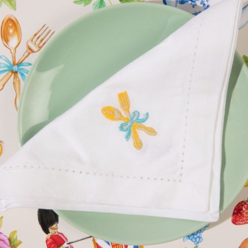 A folded white cotton napkin with fork and spoon embroidered in the corner, tied with a pretty blue bow 