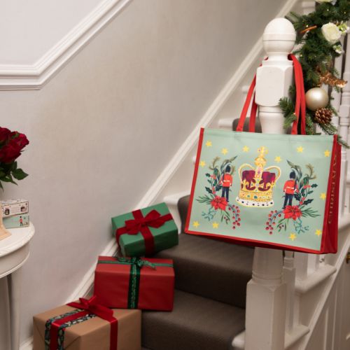 tote bag with crown, gaurdsman and christmas florals decorated with stars on a green background and red piping and handles.