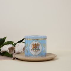 Blue tin tea caddy decorated with the Royal Coat of Arms, a crown, foliage with ribbons and a touch of gold.