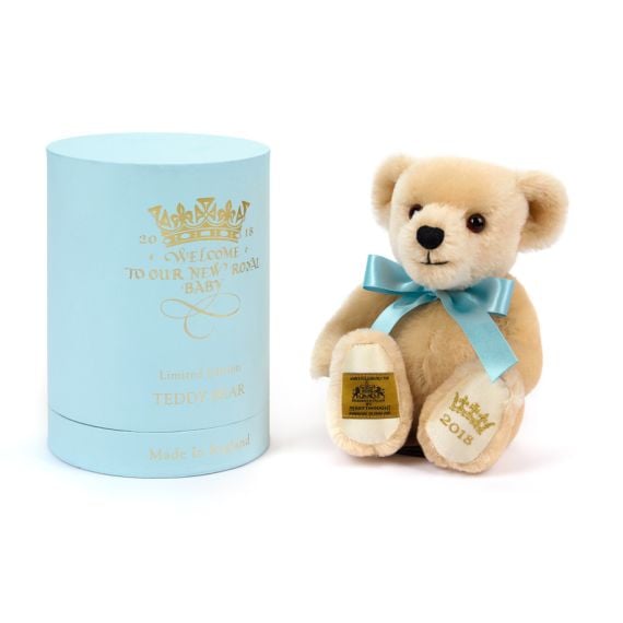 Merrythought bear with blue bow and paw embroidered with crown and year, 2018 next to blue presentation box. 