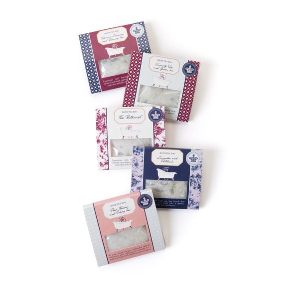 Five boxed bath tea bag products arranged in a staggered layout on a light background, each with decorative floral packaging in different colour schemes (burgundy, blue, pink, and white) and a small window showing the bath tea bags inside.