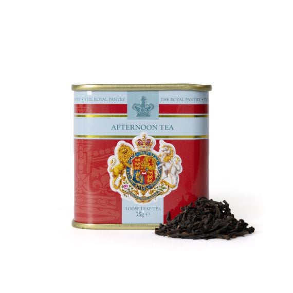 Tin of Afternoon Tea from The Royal Pantry, featuring a red and pale blue design with the Royal Coat of Arms and crown motif. The gold-lidded tin contains 25g of loose leaf tea, with a small pile of dark tea leaves displayed beside it.