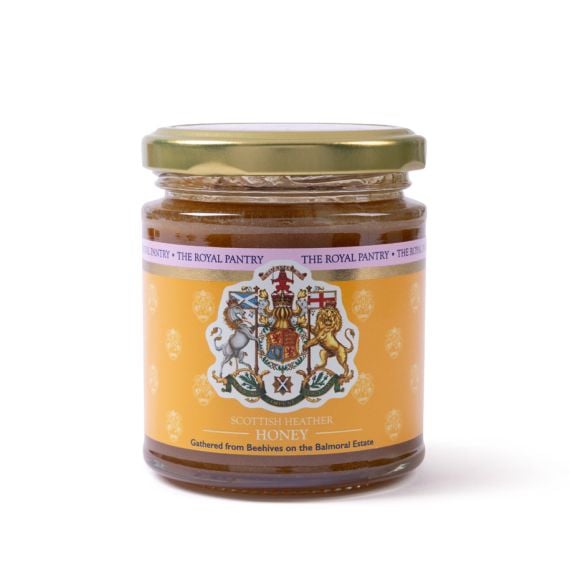 Front view of a glass jar of Scottish Heather Honey from The Royal Pantry, featuring a gold lid and an amber label decorated with the Royal Arms of Scotland. The honey is gathered from beehives on the Balmoral Estate.