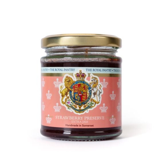 Glass jar of strawberry preserve with a gold-coloured lid, featuring a pink label decorated with the Royal Coat of Arms and crown motifs. The label reads "Strawberry Preserve Extra Jam" and "Handmade in Somerset."