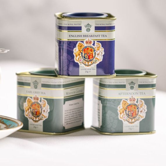 Three loose leaf tea caddies from The Royal Pantry arranged on a light surface, featuring English Breakfast Tea, Earl Grey Tea and Afternoon Tea. The decorative tins display the Royal Coat of Arms and are stacked with the English Breakfast Tea caddy balan