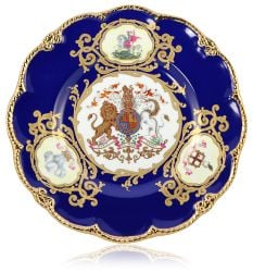 English fine bone china Prince William Plate with a design featuring a royal coat of arms surrounded by three other royal representations on a deep blue background and guilded rims. Includes a presentation gift box. 