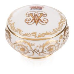 Circular white pillbox with intricate gold detail and the Victoria and Albert cipher on the lid under the coronet