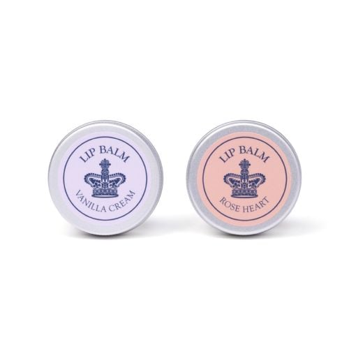 Two lip balm tins with silver lids and crown design, labelled Vanilla Cream (lilac) and Rose Heart (peach), displayed on a light background.