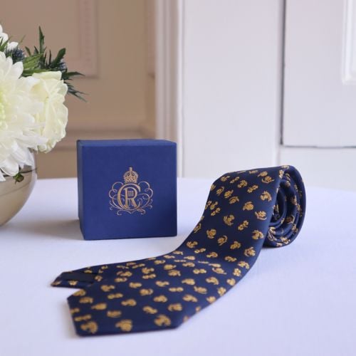 Close up image of our 100% woven silk tie in navy blue and burnished gold with floral motifs from the four nations of the United Kingdom - thistle, rose, shamrock and daffodil .